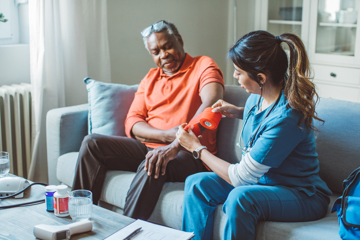 Female caregiver bandaging older man's arm