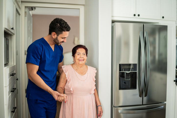 Caregiver walking older woman into kitchen